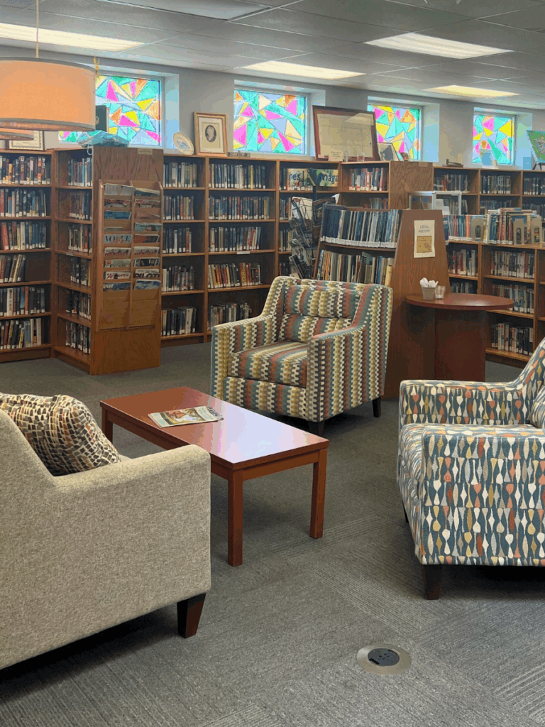 Inside of a public library, the photo features many bookshelves and comfortable seating for library visitors.