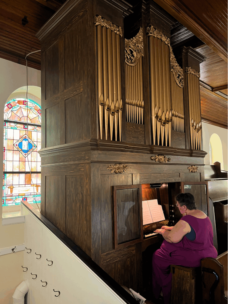 A woman plays a Kantner organ in a church with stained glass windows.