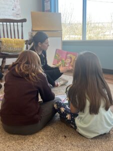 A volunteer medical student interested in pediatric dental care reads a book about oral health to an audience of children.